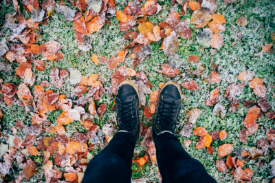Person standing over grass and leaves with a layer of frost.