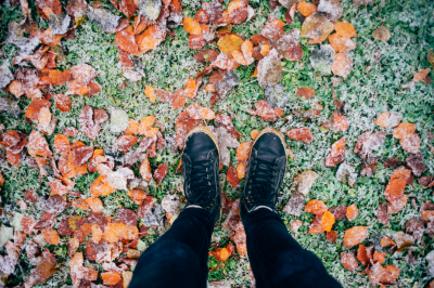 Person standing over grass and leaves with a layer of frost. Person standing over grass and leaves with a layer of frost.